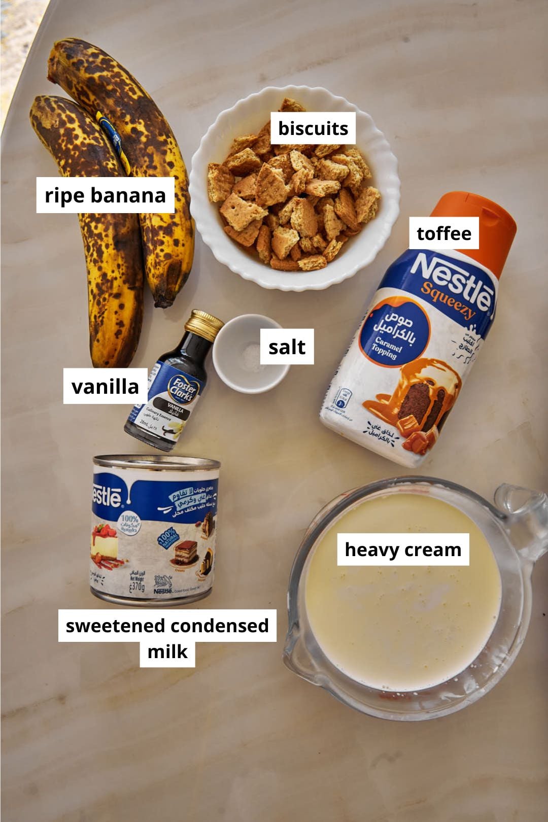 labeled ingredients needed to make banoffee ice cream on a white marble background.
