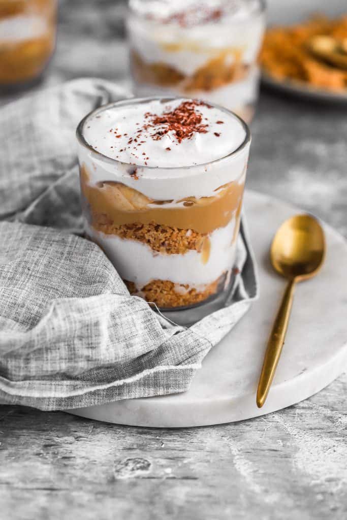 close up pic of a banoffee cup on a gray kitchen cloth with a gold spoon
