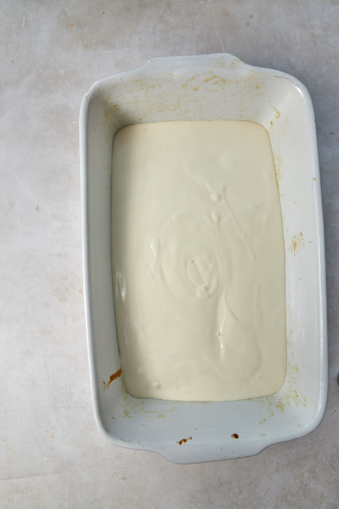 cream layer spread onto basbousa layer in a white baking dish.