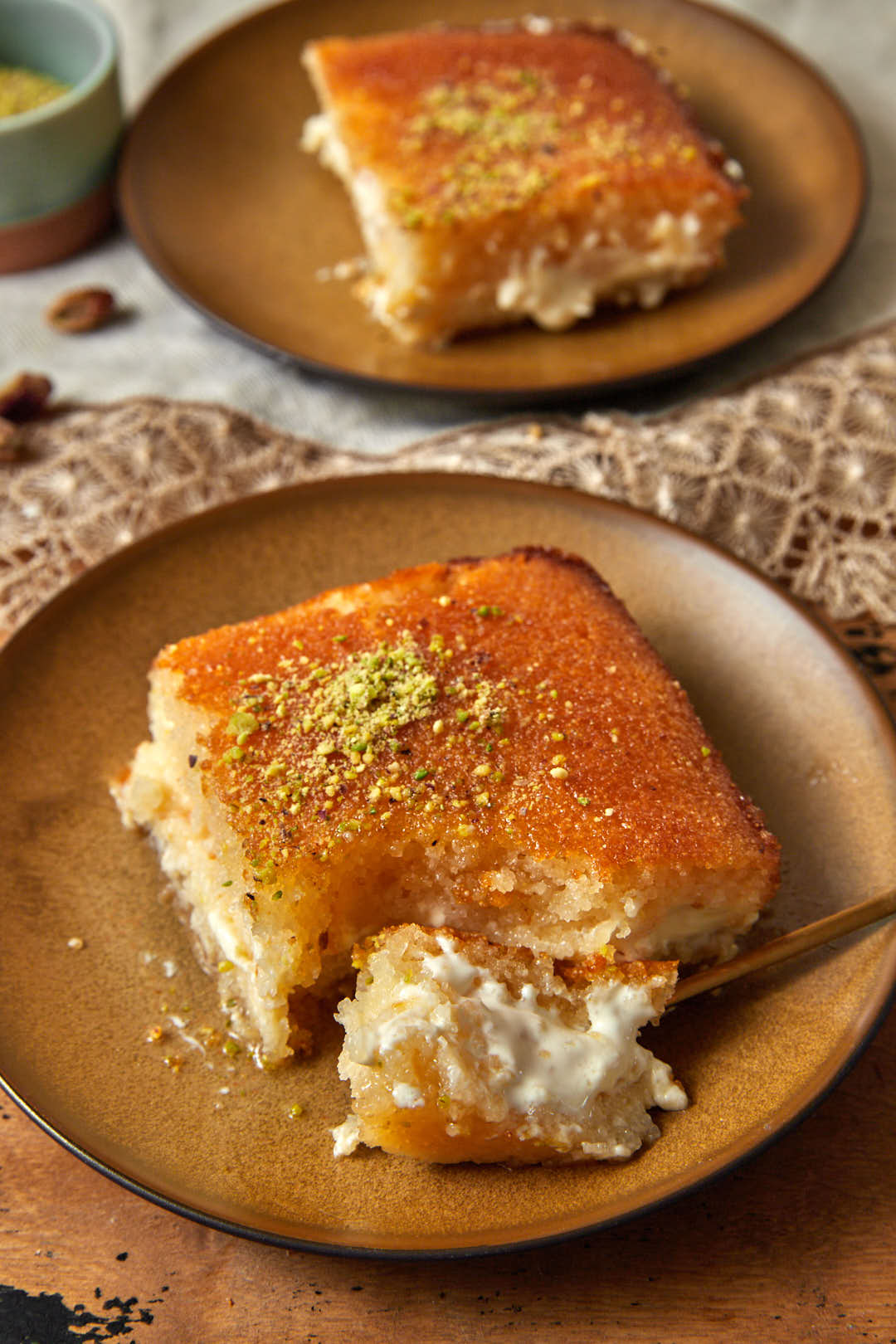 a slice of basbousa with a fork taking a bite out, with another slice on a plate in the background.