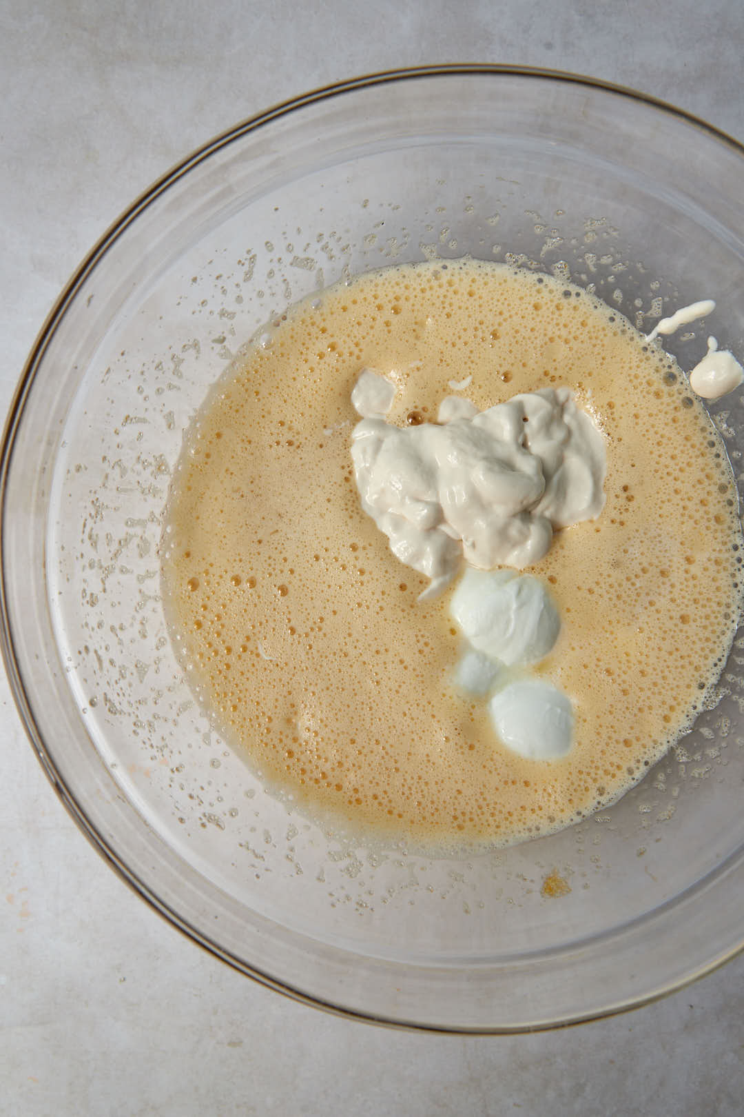 yogurt and cream added to beaten eggs and sugar in a glass bowl.