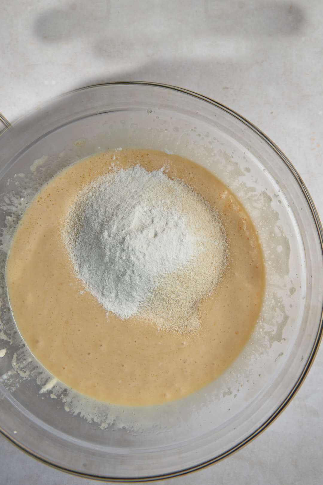 semolina and baking powder added to wet ingredients in a glass bowl.