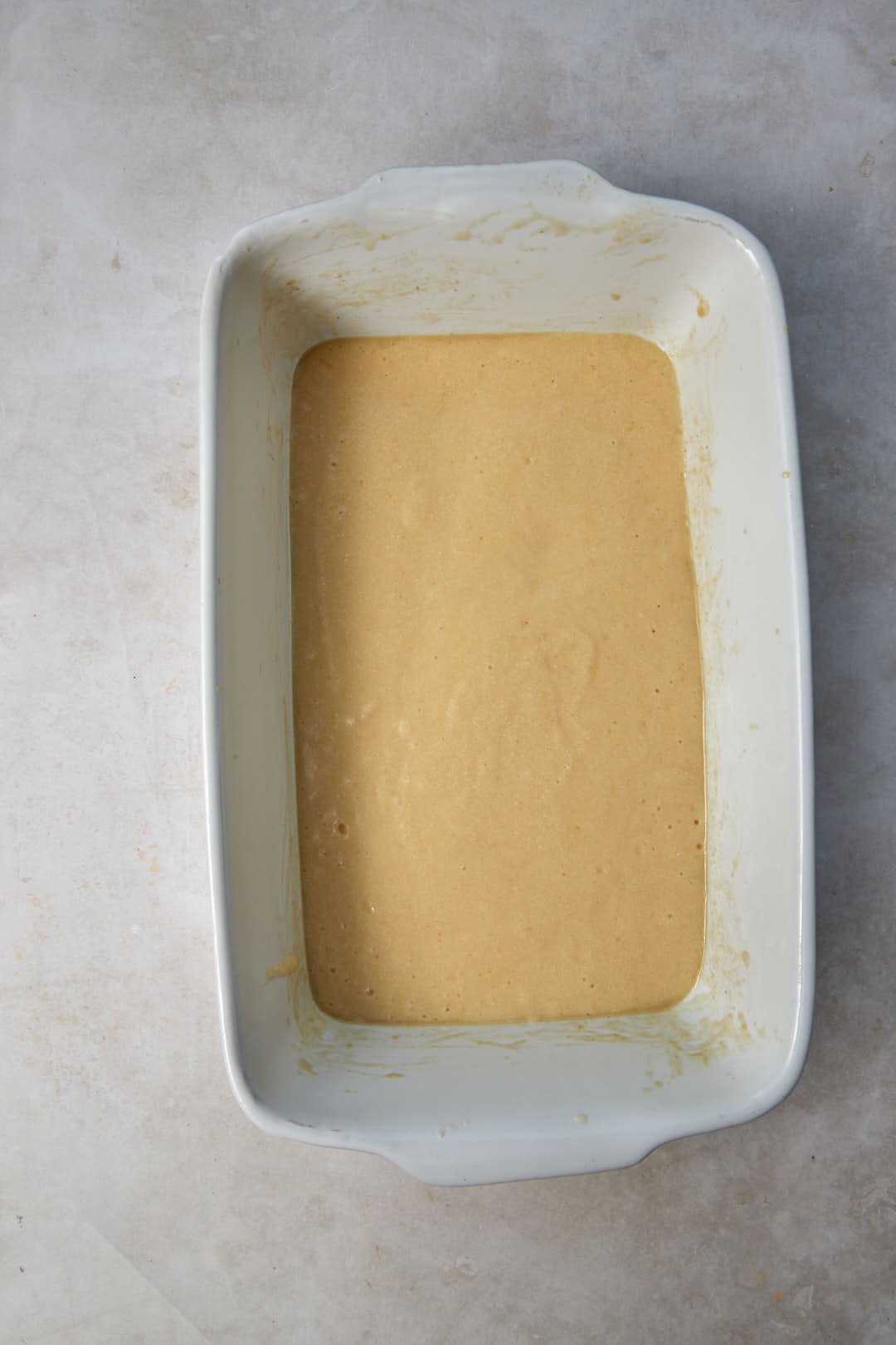 white baking pan with half basbousa batter poured in it.