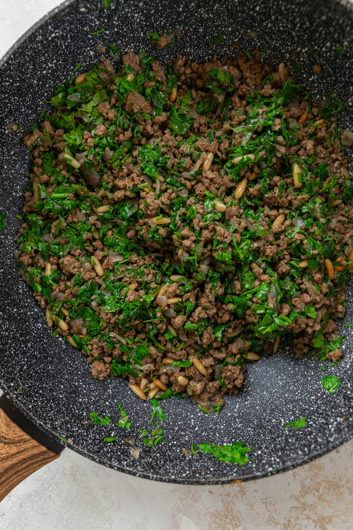 ground beef in skillet with onions and pine nuts.