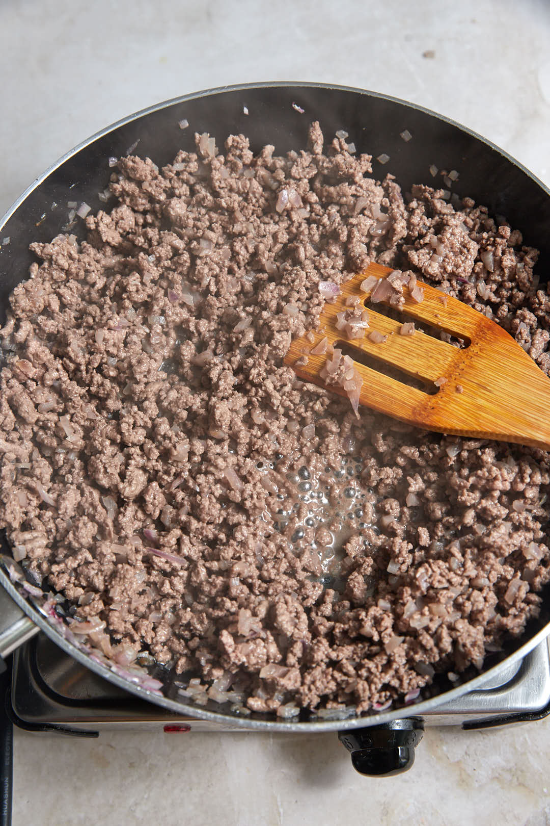 cooked ground beef in a skillet with a wooden spatula.