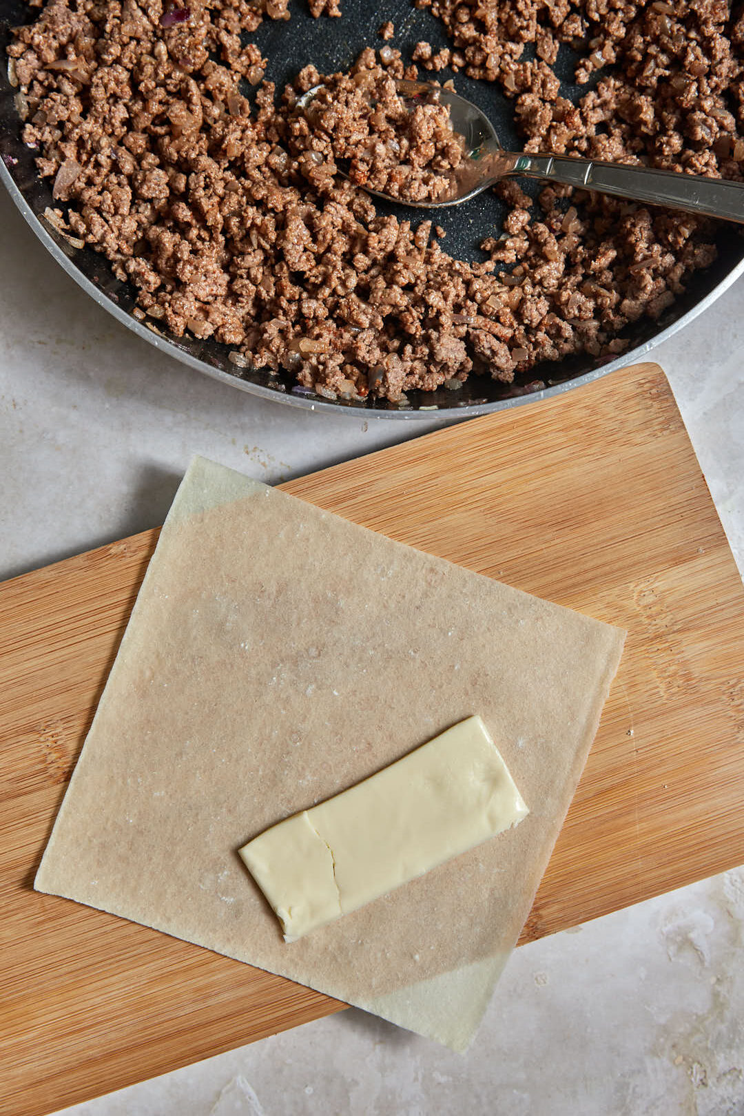 slice of american cheese in a spring roll wrapper with ground beef in a skillet.