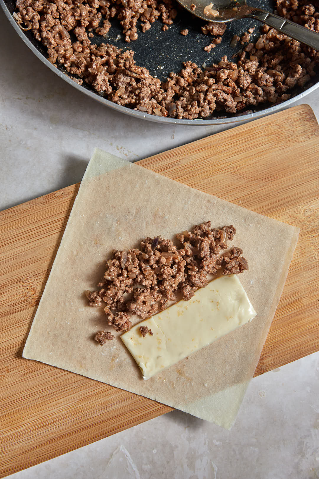 ground beef added to a spring roll wrapper on a wooden board.