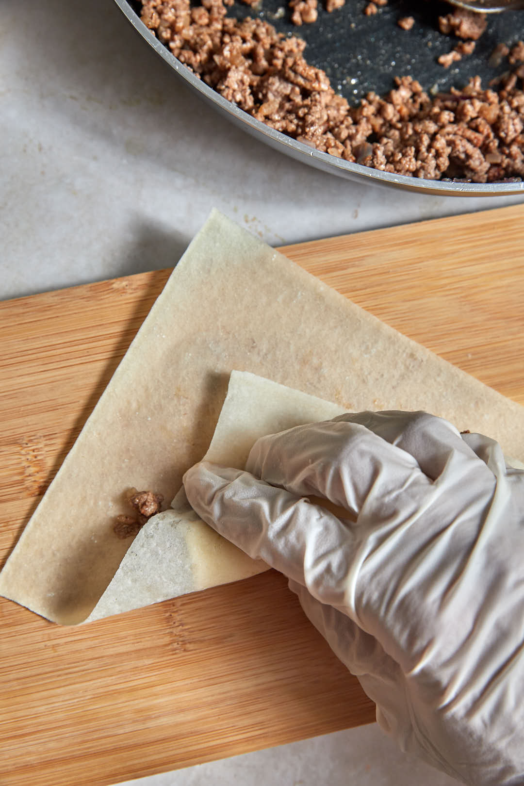 spring roll wrapper being folded over cheeseburger filling.