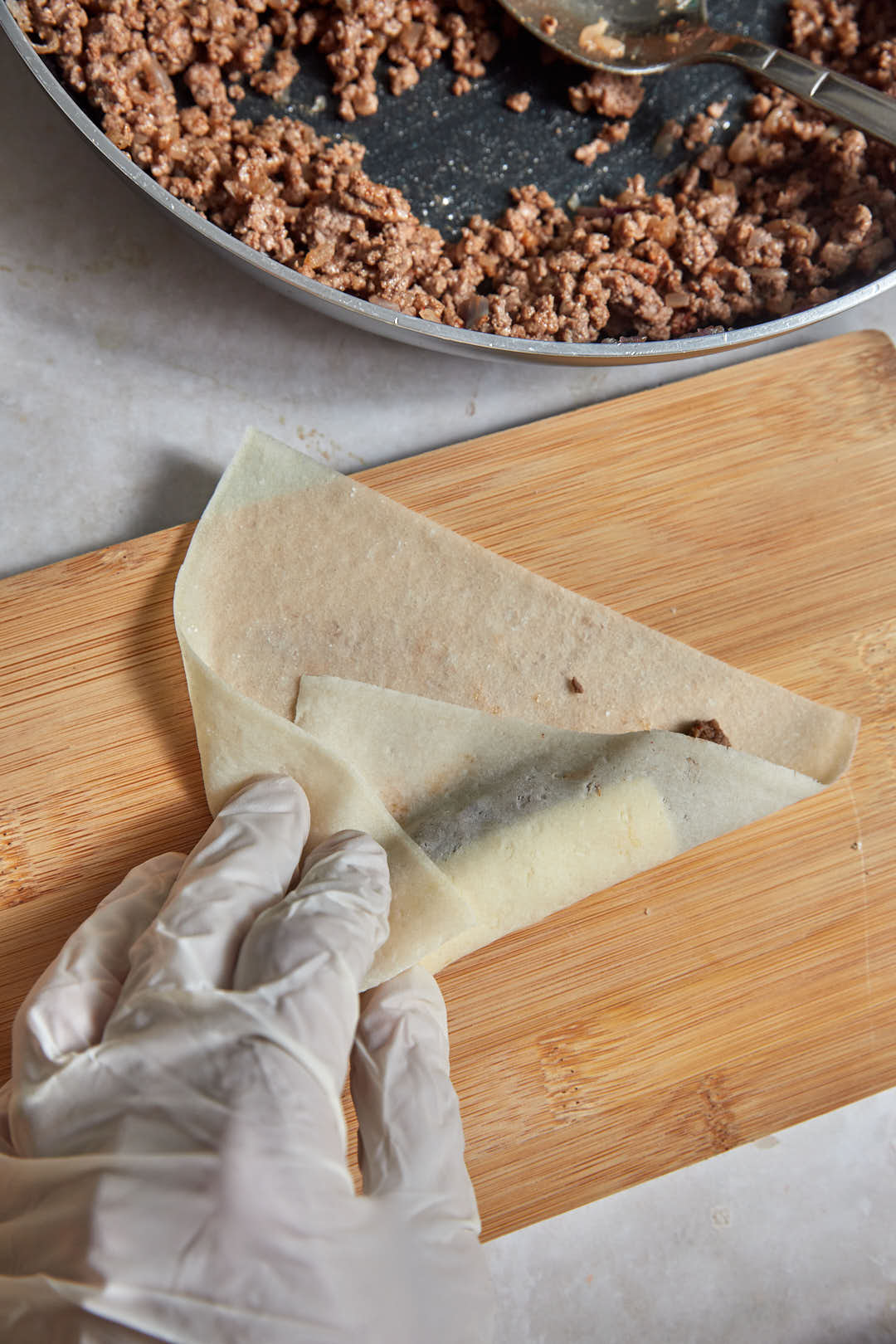 spring roll wrapper being folded over cheeseburger filling.
