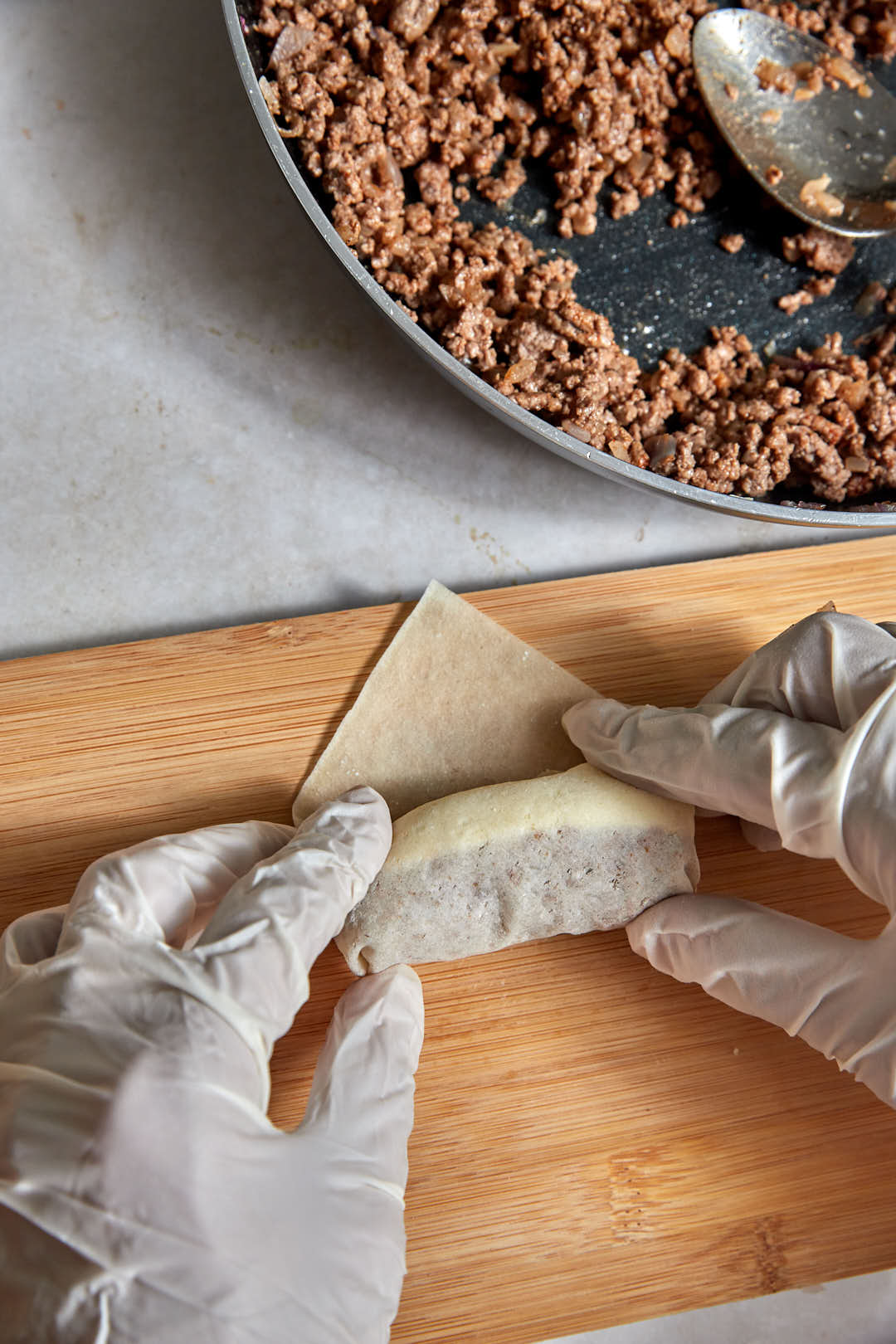 cheeseburger spring roll being rolled on a wooden board.