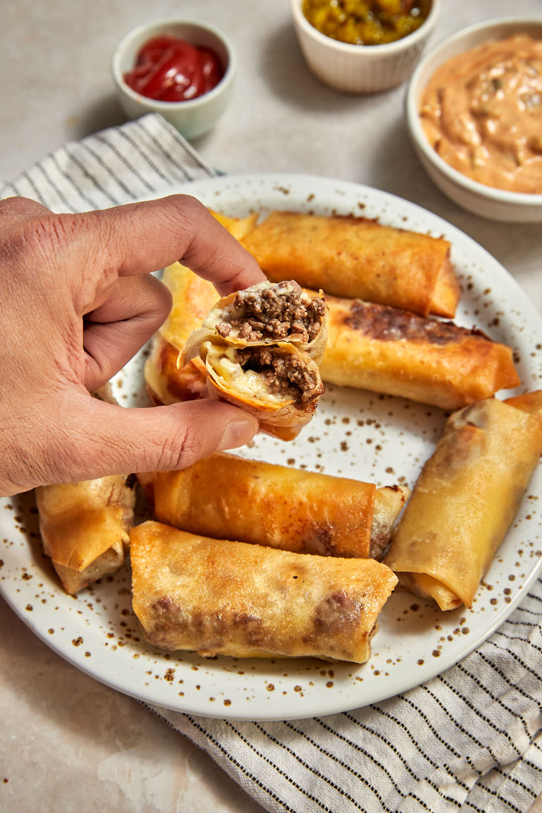hand holding a halved big mac spring roll over a plate.