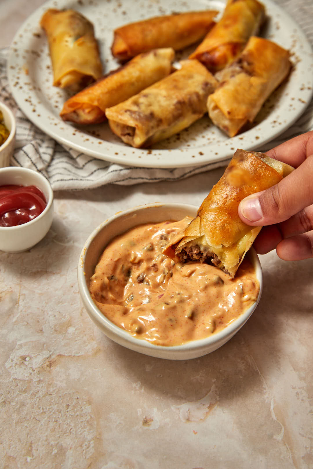 a cheeseburger spring roll being dipped into big mac dipping sauce in a small bowl.