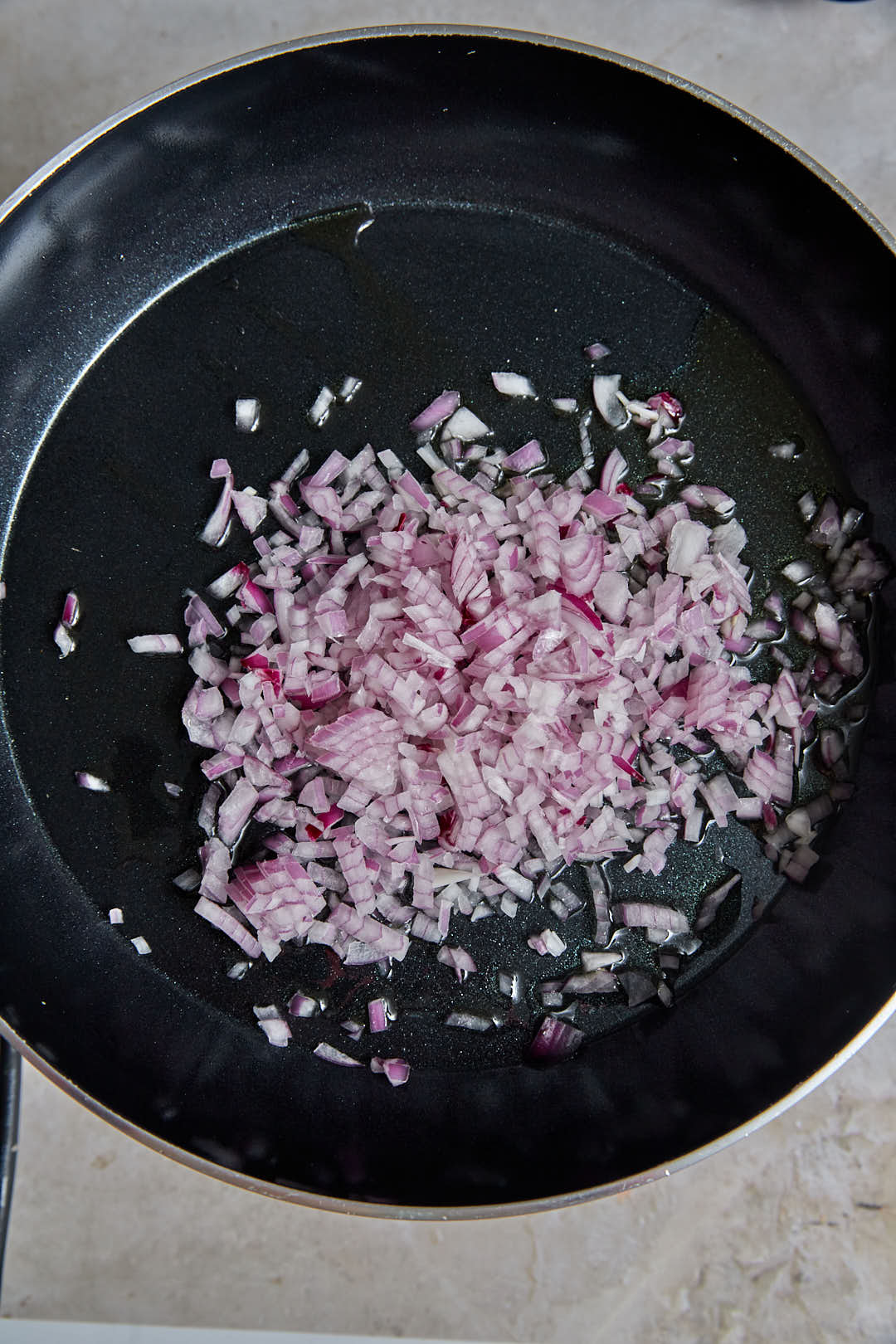 finely diced red onions being sauteed in a large skillet.