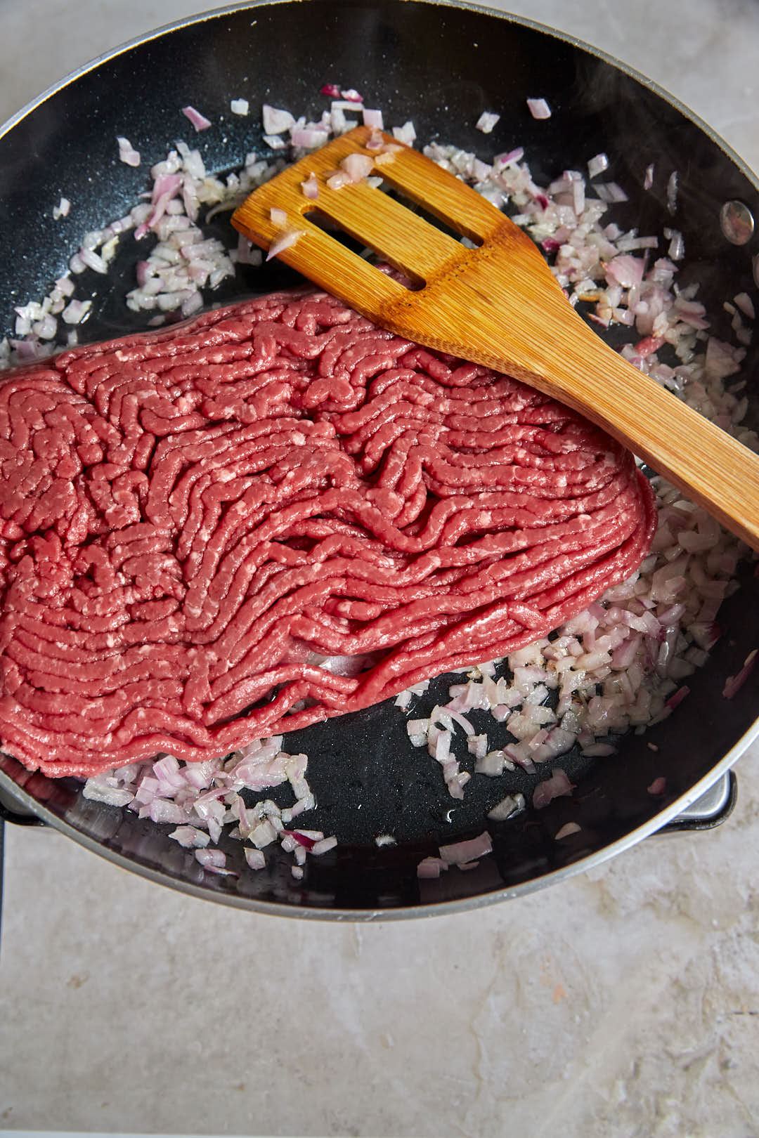 raw ground beef in a skillet with softened diced onions.