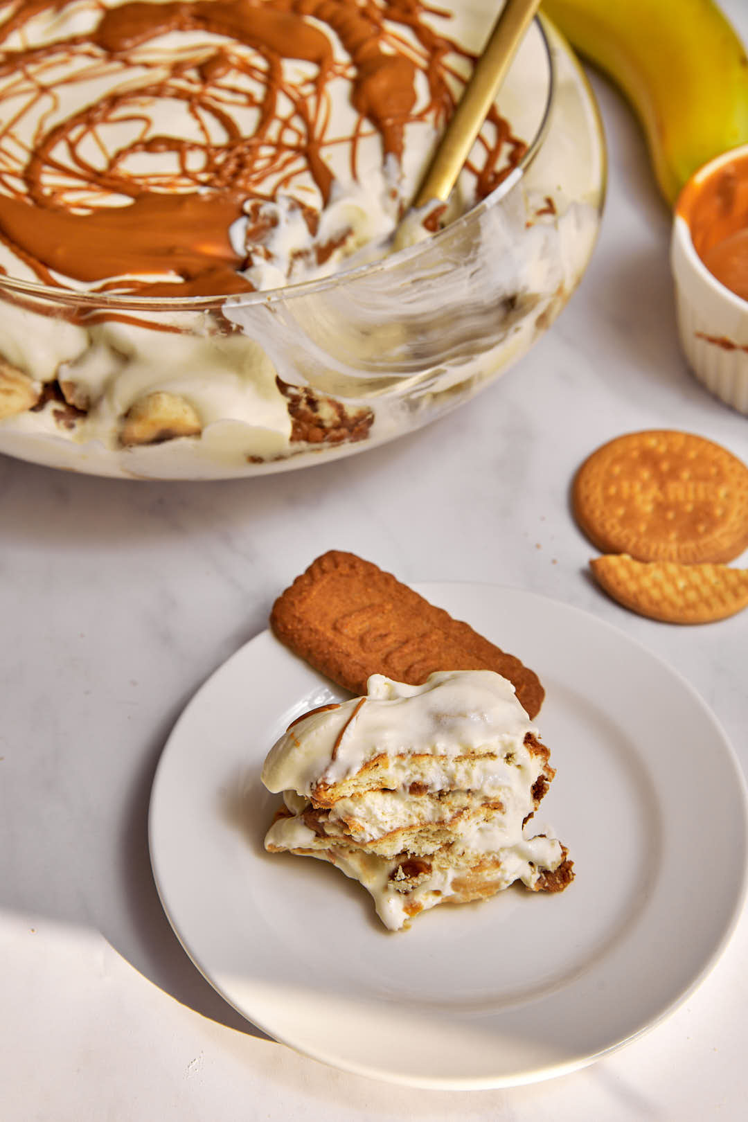 biscoff banana pudding on a white plate, with the serving dish in the background.