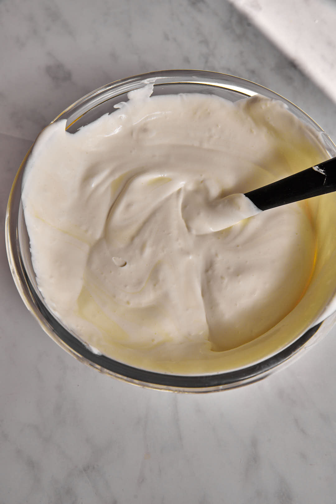 heavy cream and condensed milk folded together with a spatula in a glass bowl.