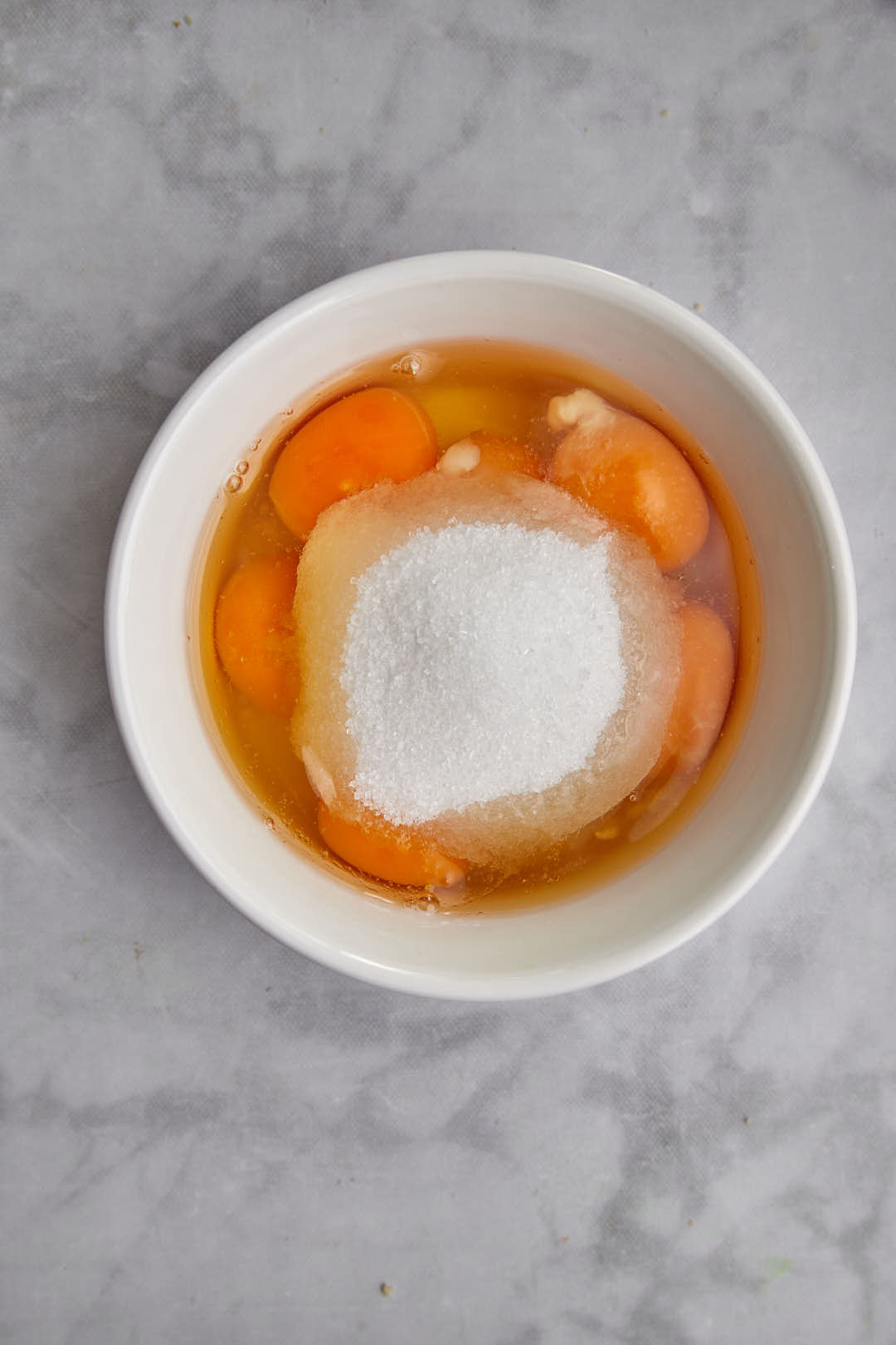 Egg, egg yolks, and white sugar in a small white bowl.