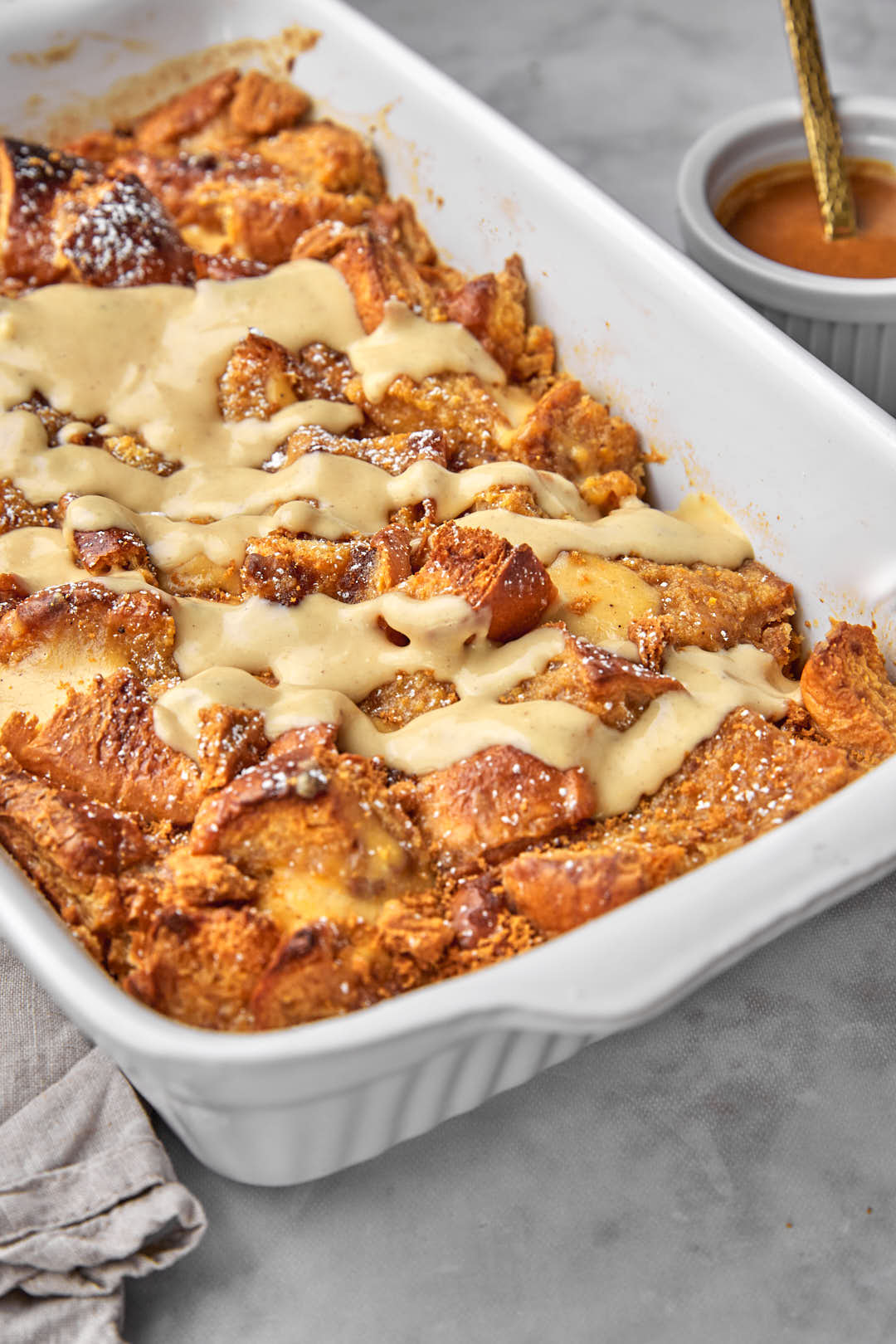 a white pan of biscoff bread pudding with extra biscoff custard drizzled on top.