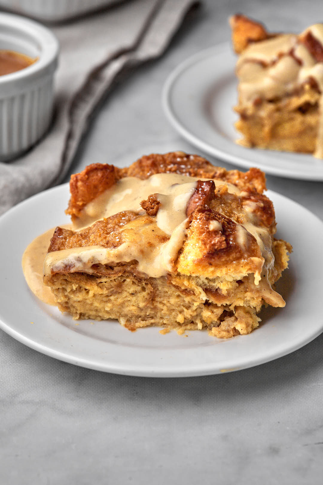 big square piece of brioche bread pudding with biscoff custard dripping off of it on a white plate.