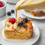 biscoff custard being poured over a slice of bread pudding in a white plate.