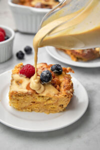 biscoff custard being poured over a slice of bread pudding in a white plate.
