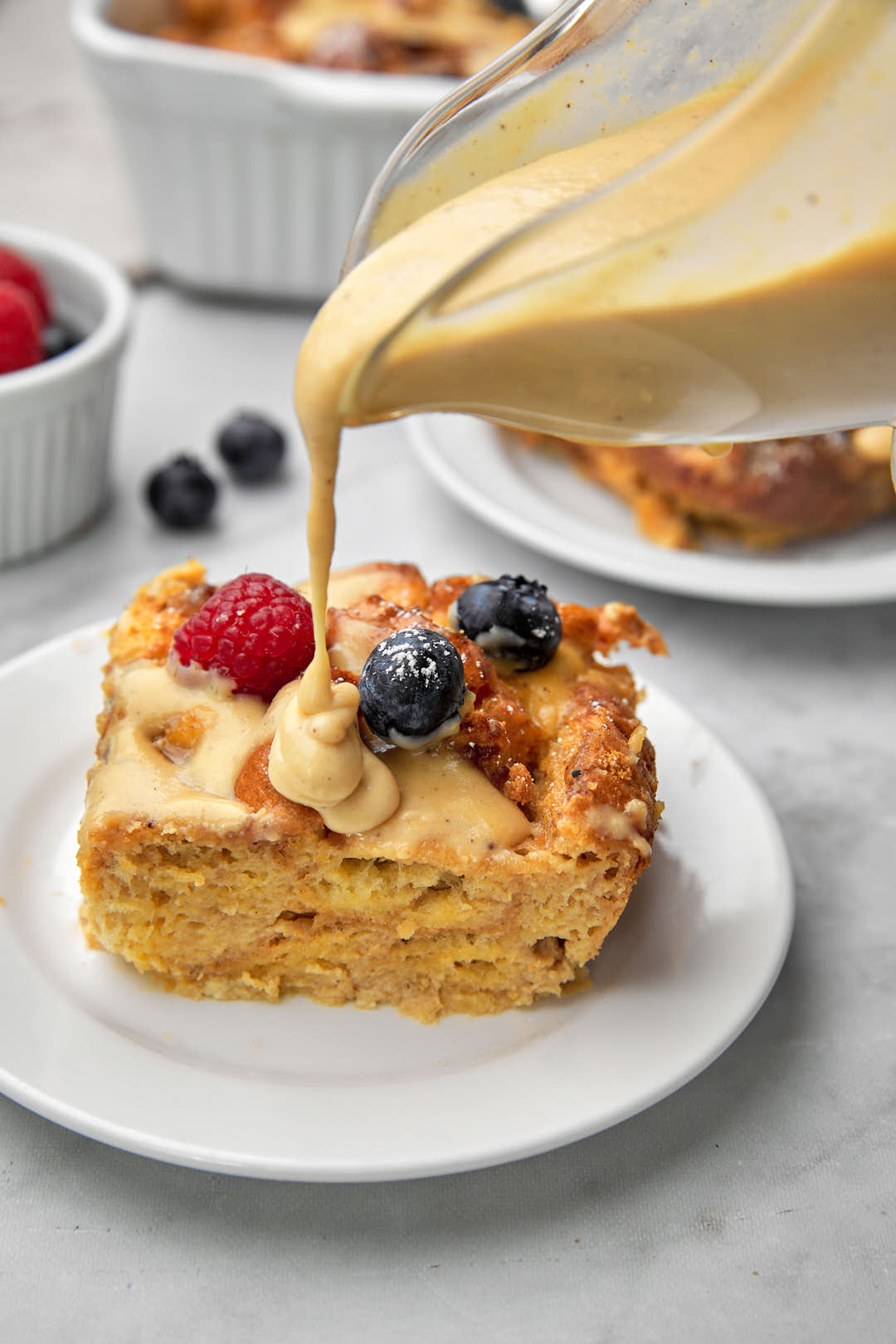 biscoff custard being poured over a slice of bread pudding in a white plate.