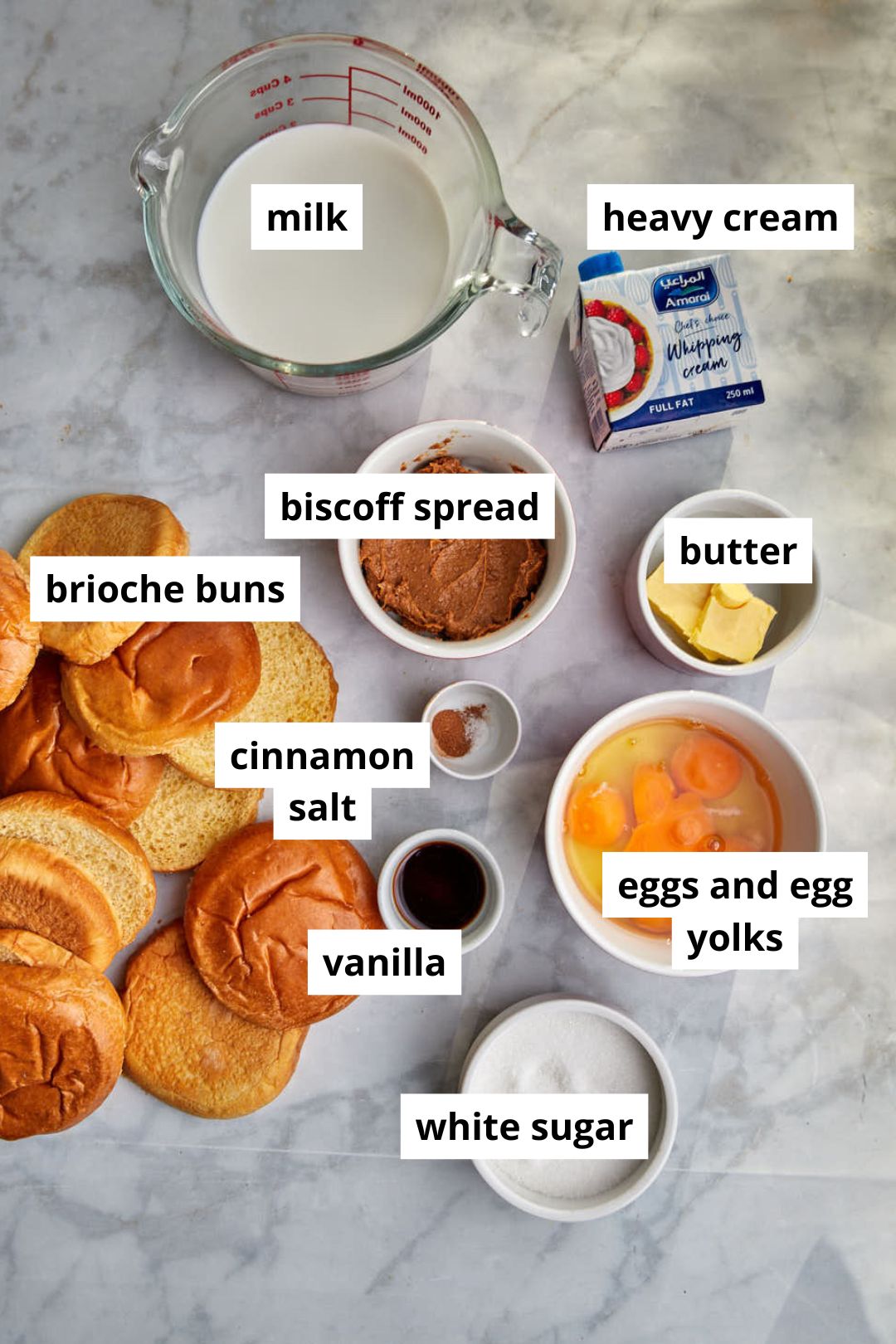 ingredients for biscoff bread pudding on a white marble backdrop.