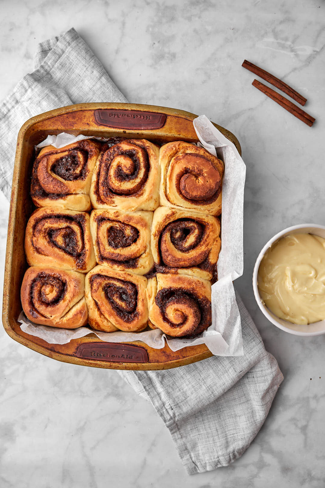 baked cinnamon rolls in a pan with cream cheese frosting on the side.