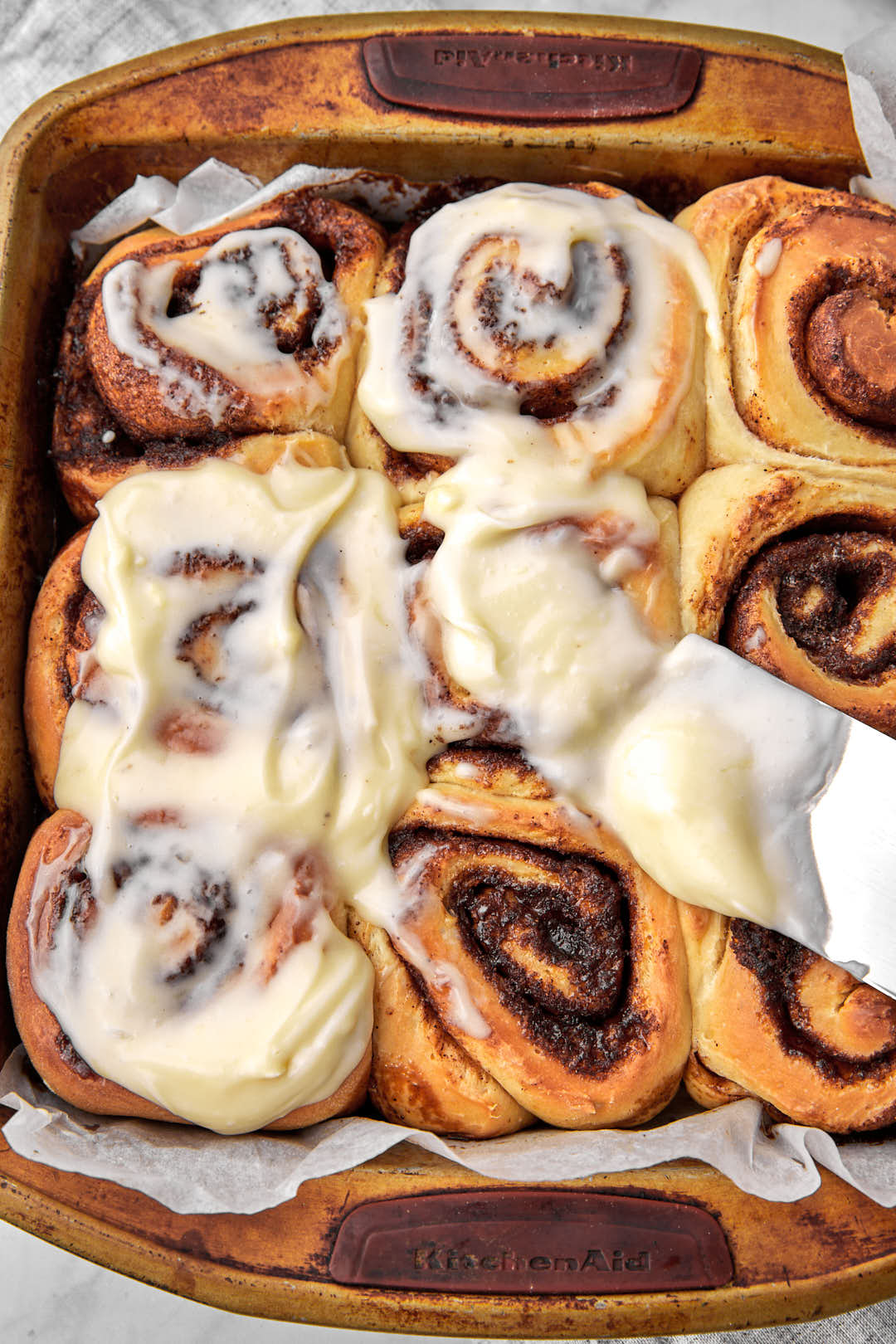 cream cheese frosting being spread onto cinnamon rolls after baking.