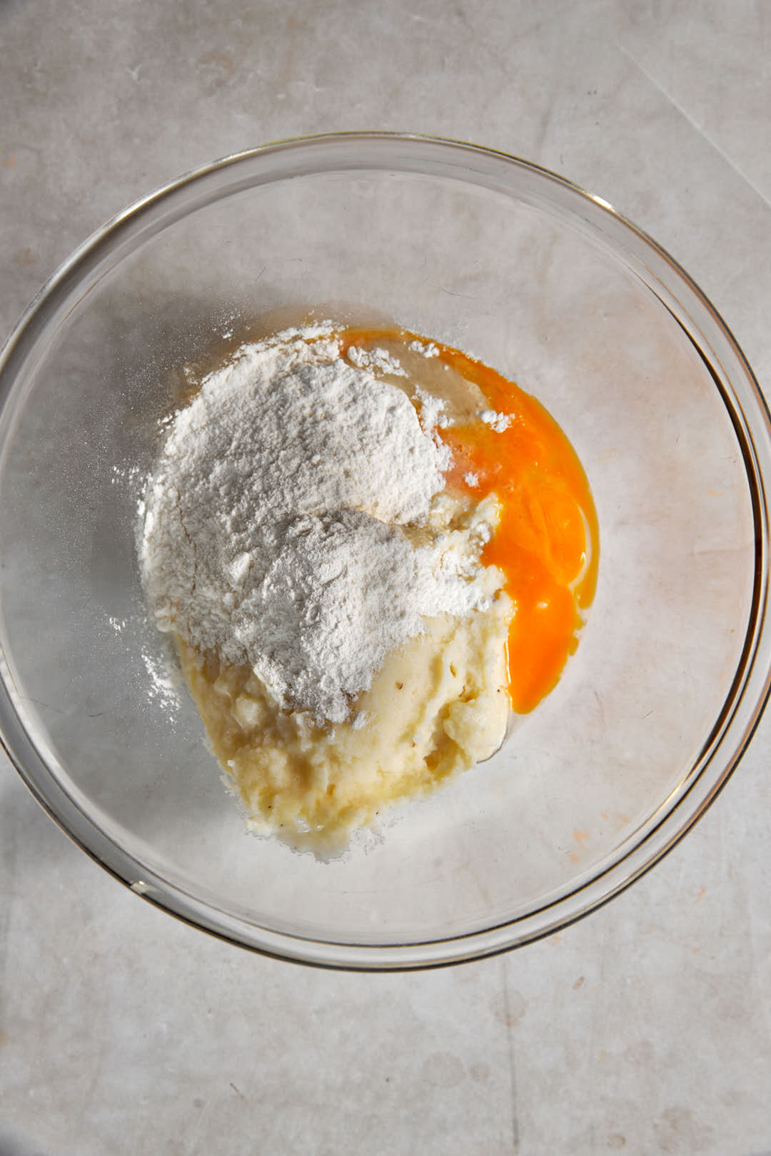 mashed potatoes, egg, and flour added to a glass bowl.