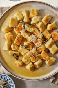 a plate full of brown butter gnocchi in a brown butter sauce with sage and parmesan cheese.