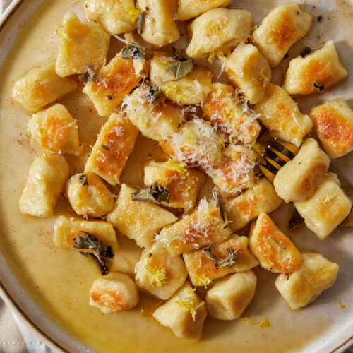 a plate full of brown butter gnocchi in a brown butter sauce with sage and parmesan cheese.