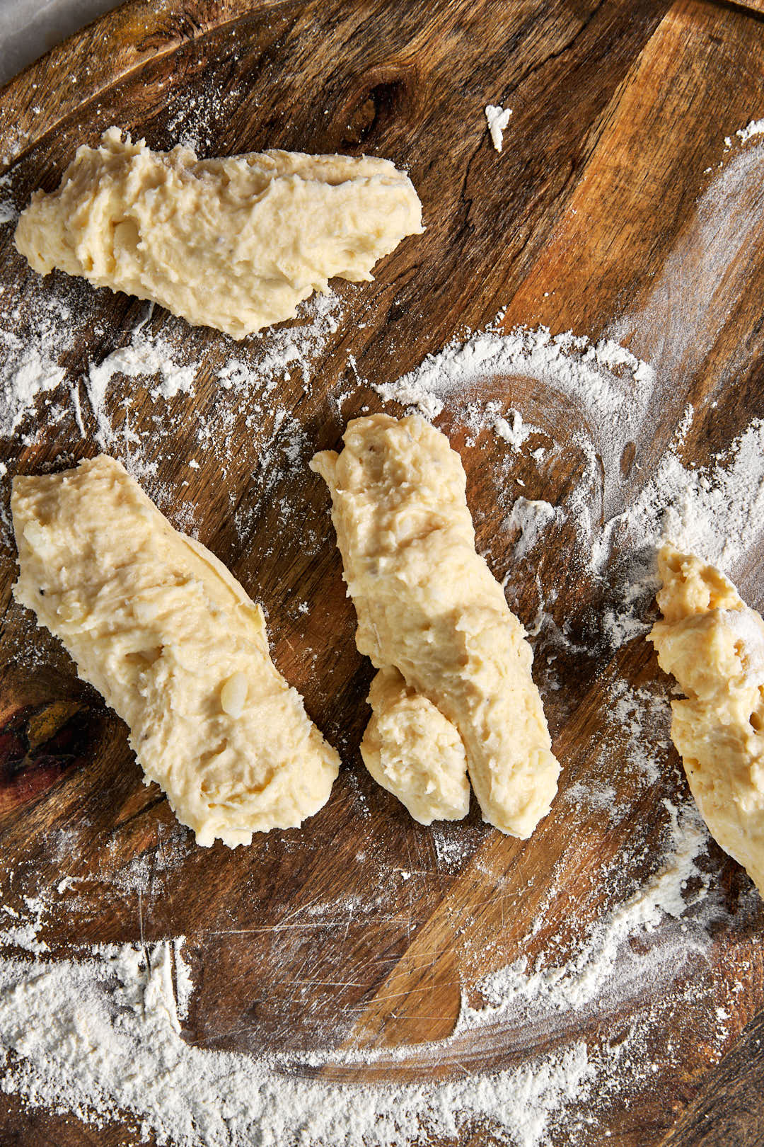 four gnocchi logs on a floured wooden surface.