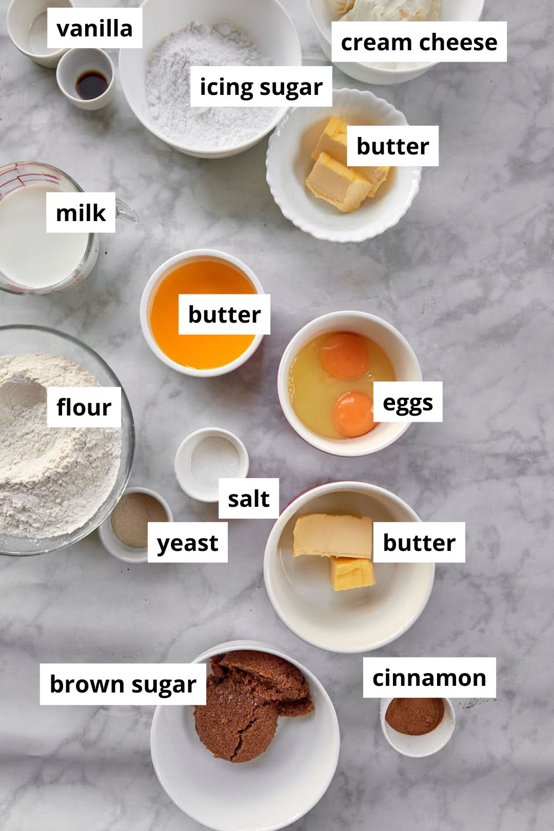 ingredients needed to make brown butter cinnamon rolls on a marble background.
