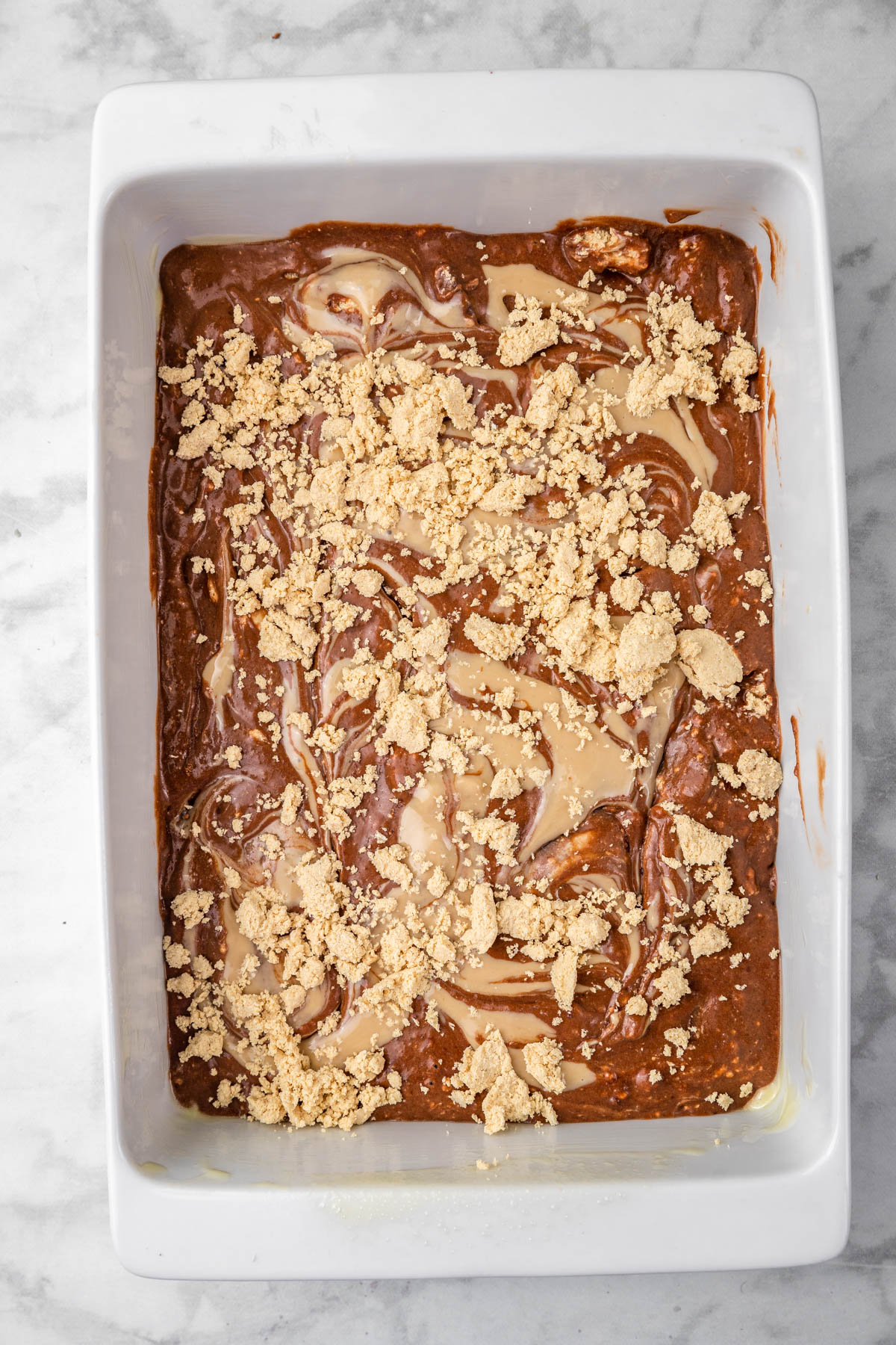 halva crumbles over chocolate cake batter in baking pan.