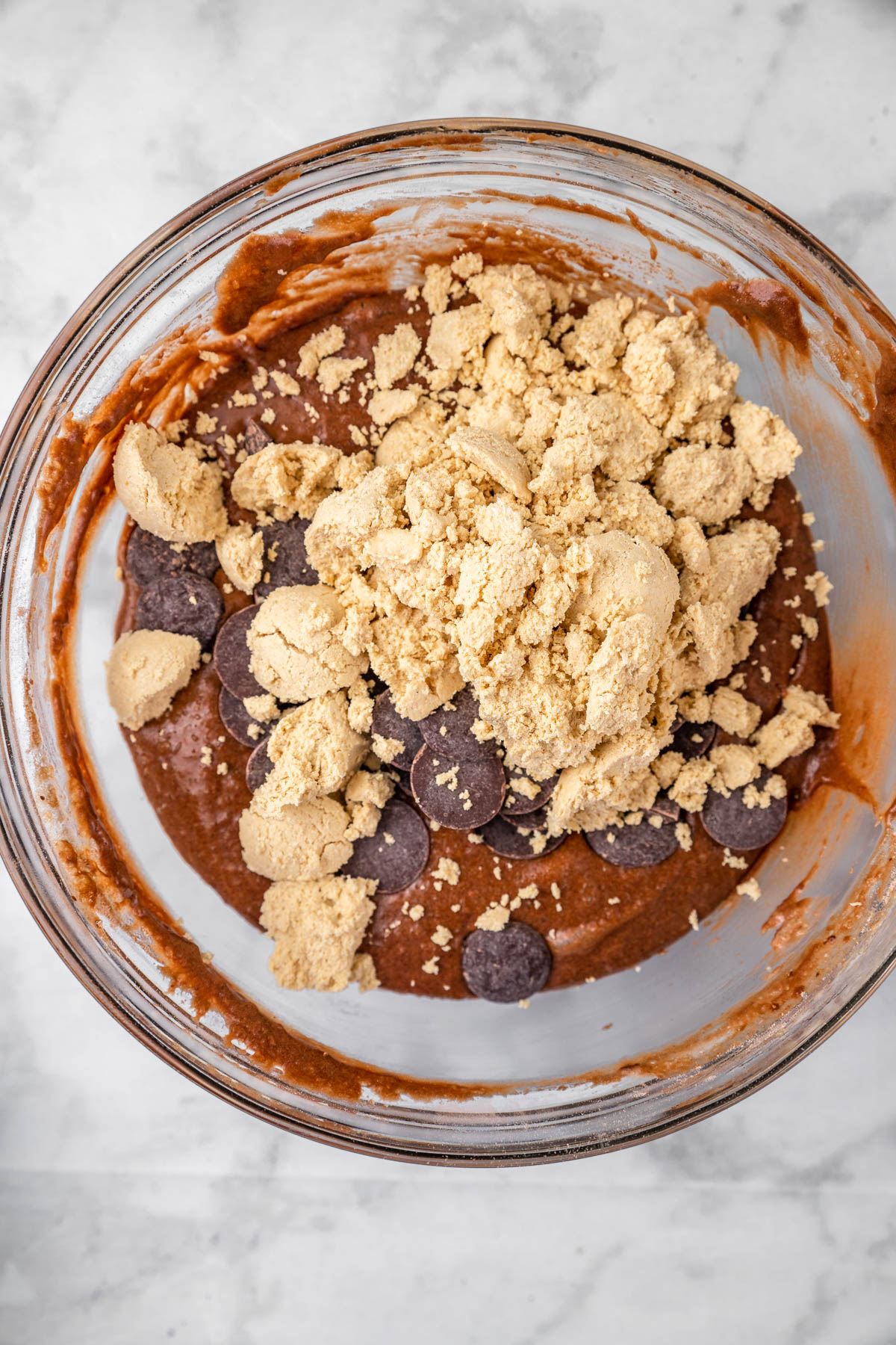 Halva chunks and chocolate chips added to chocolate cake batter in a glass bowl.