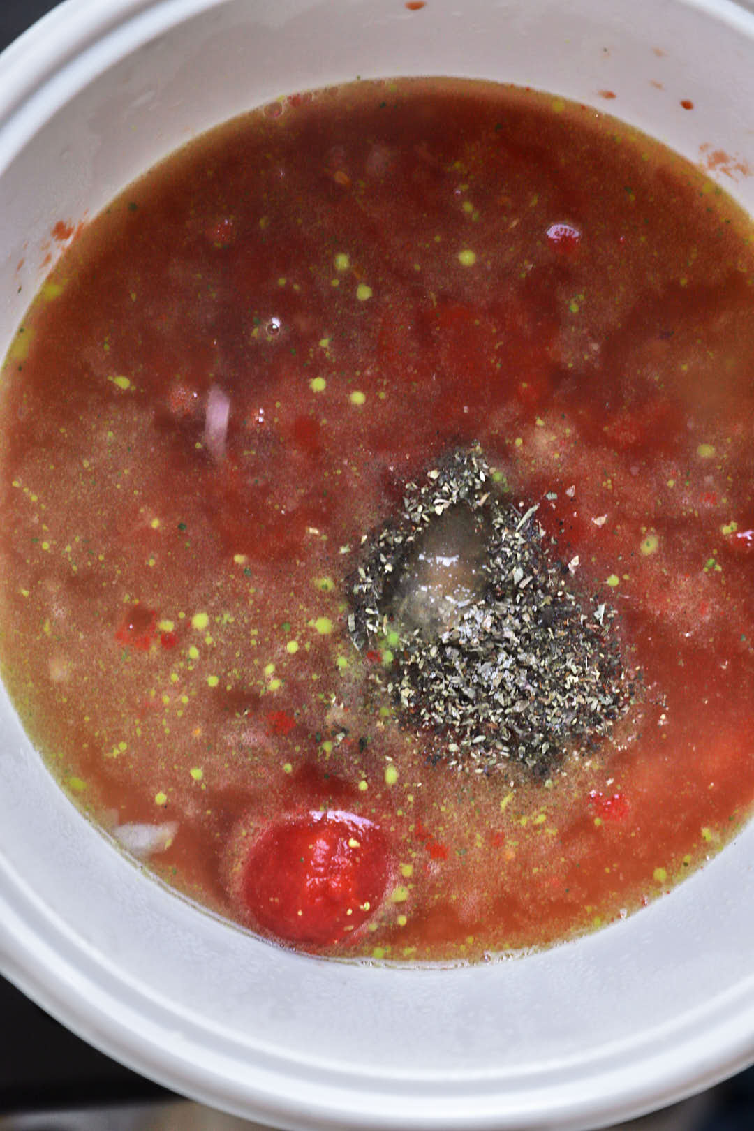 canned tomatoes and spices added to a white saucepan.