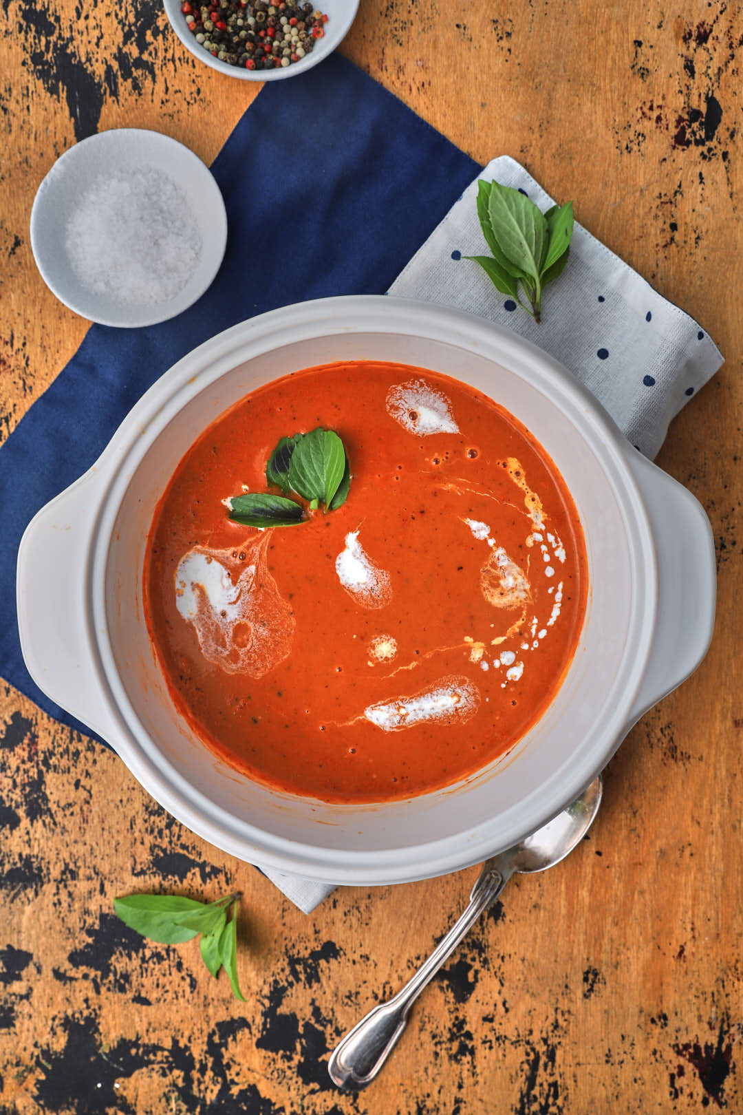 creamy tomato soup in a white saucepan with basil as a garnish on a wooden background.