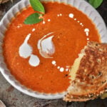 grilled cheese sandwich half resting on a bowl of tomato soup.