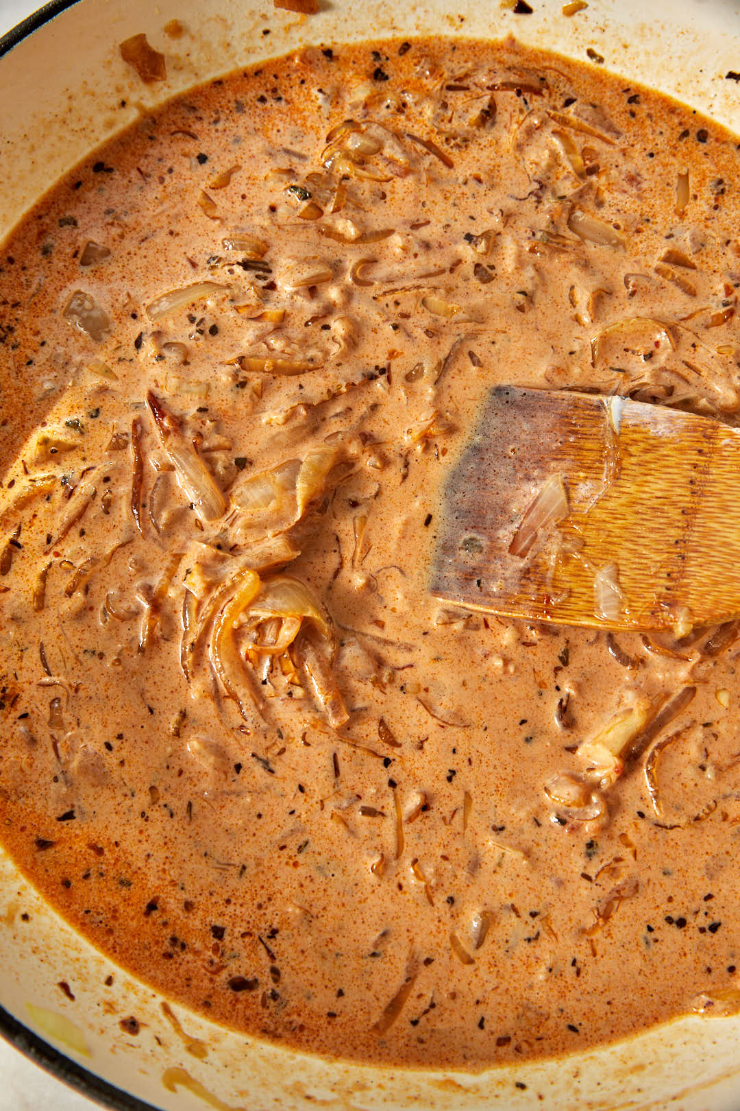creamy caramelized onion sauce stirred together in a skillet with a wooden spoon.