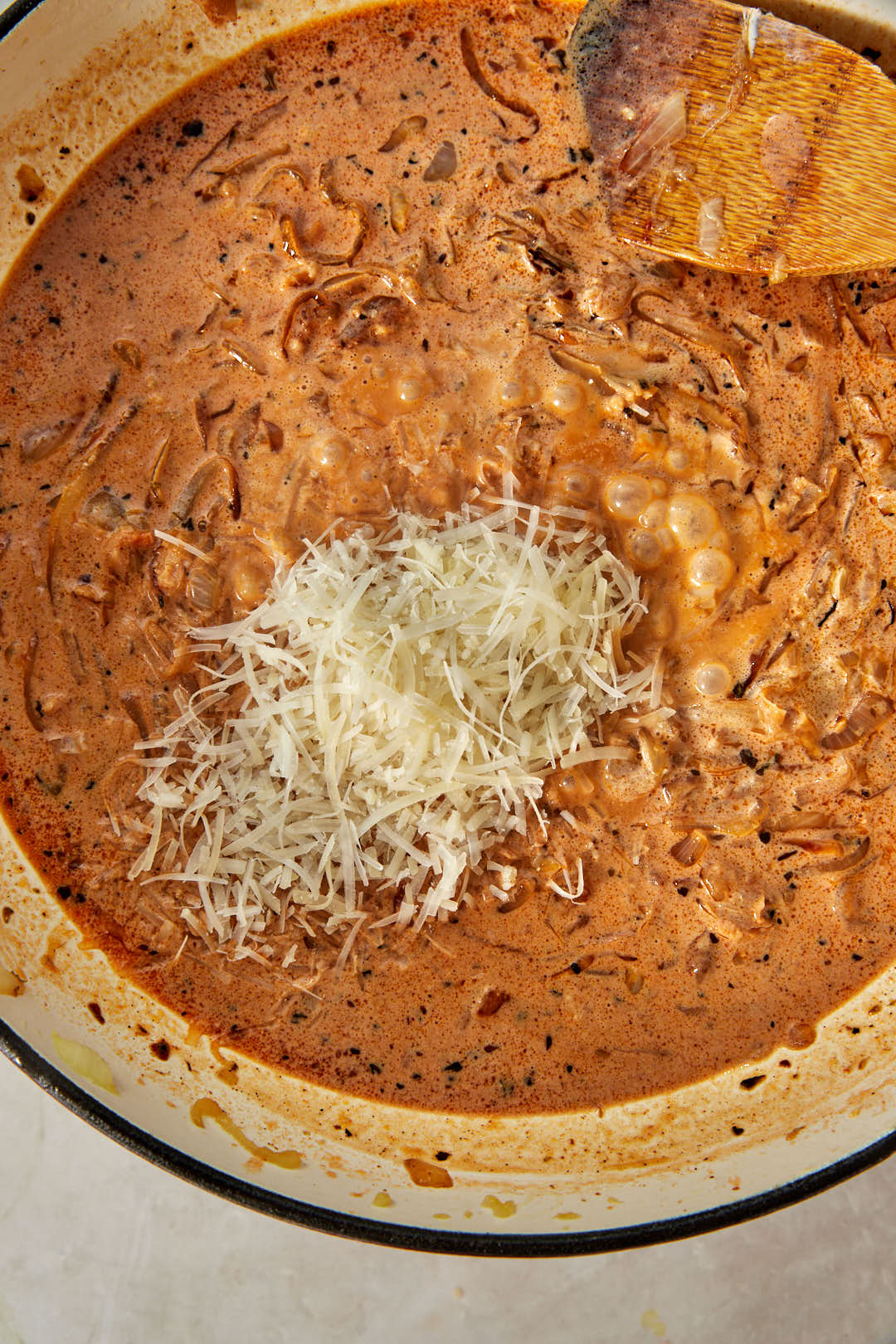 freshly grated Parmesan cheese added to creamy caramelized onion sauce in a skillet.