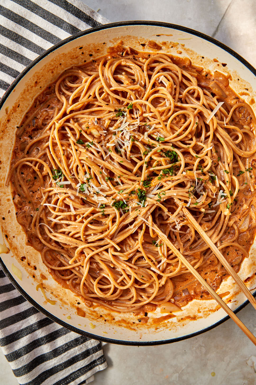 a large skillet with caramelized onion pasta in it and wooden tongs removing some.