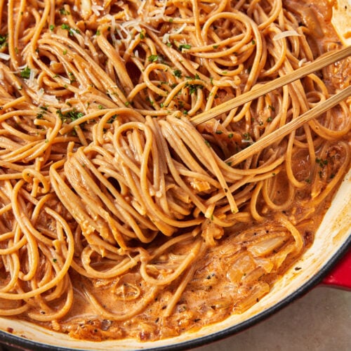 wooden tongs twirling caramelized onion pasta in a deep skillet.