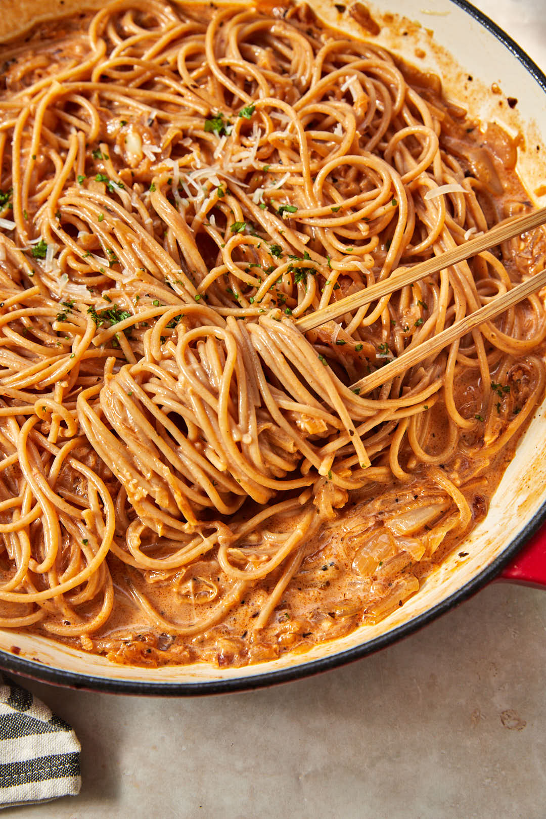 wooden tongs twirling caramelized onion pasta in a deep skillet.