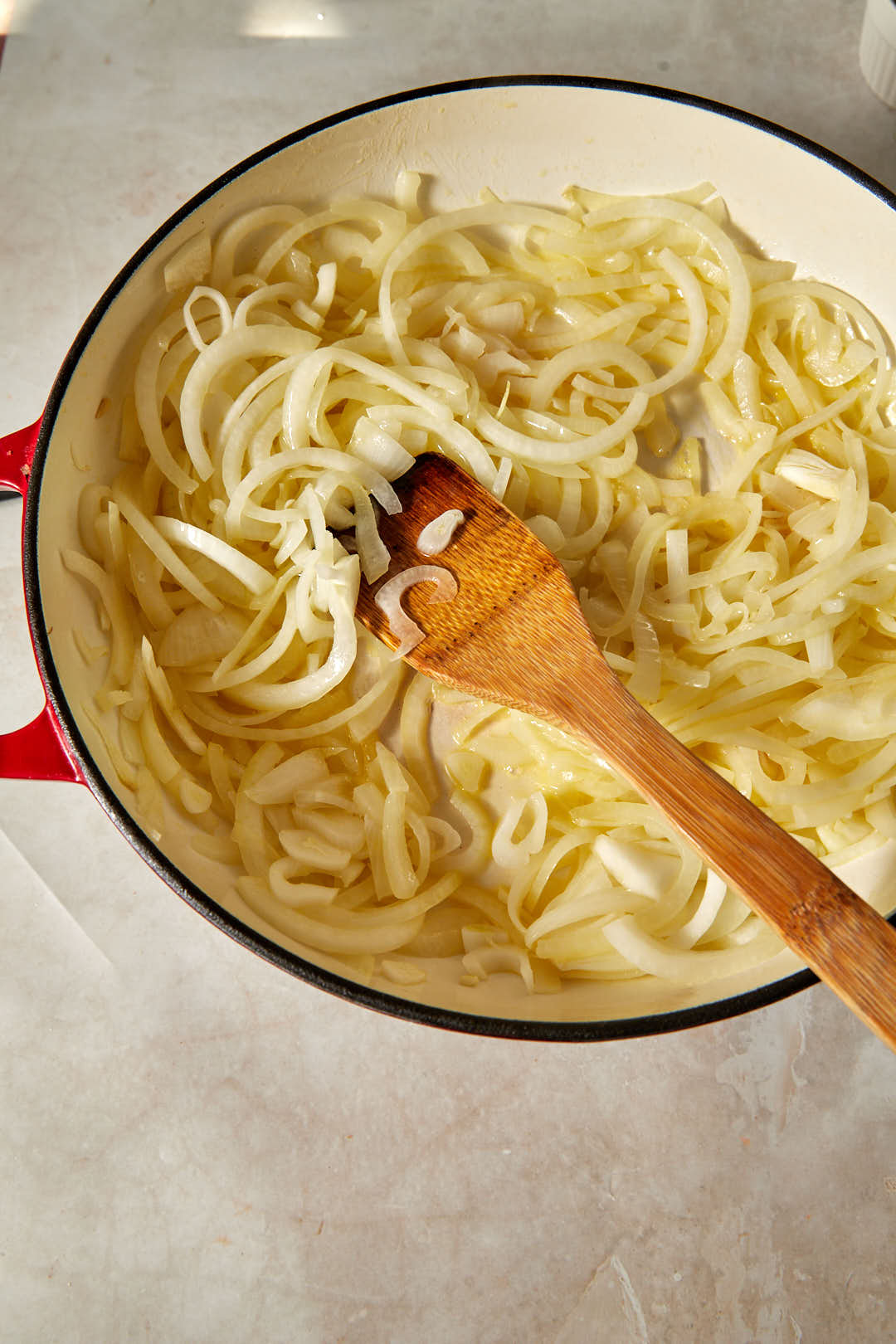 thinly sliced yellow onions added to melted butter and olive oil in a skillet with a wooden spoon.