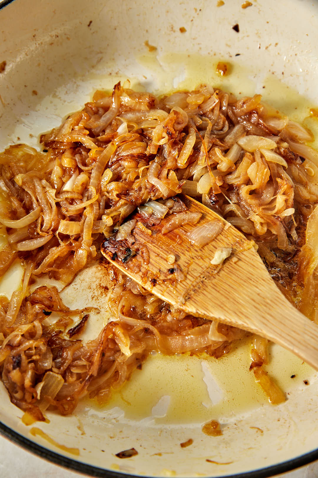 golden caramelized onions in a skillet with a wooden spoon.