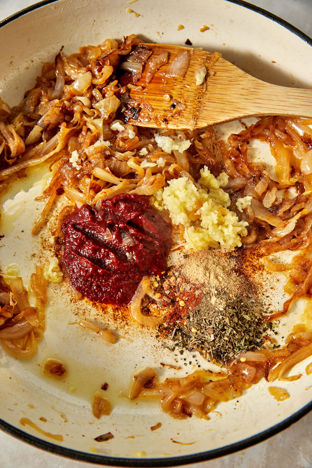 paprika, garlic powder, dried herbs and chili flakes added next to tomato paste and garlic in a skillet of caramelized onions.