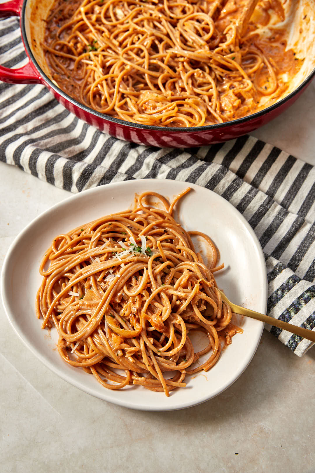 plate of caramelized onion pasta on a striped kitchen towel, with big skillet in the background.