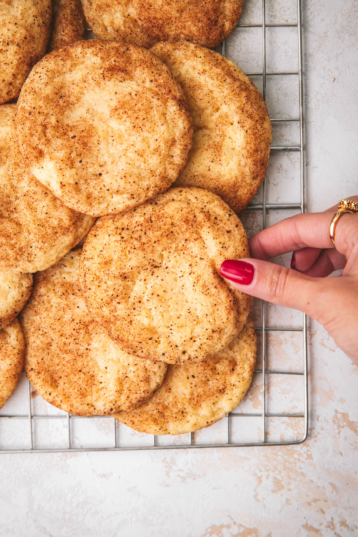 snickerdoodle cookies on baking sheet after baking with a hand grabbing one.