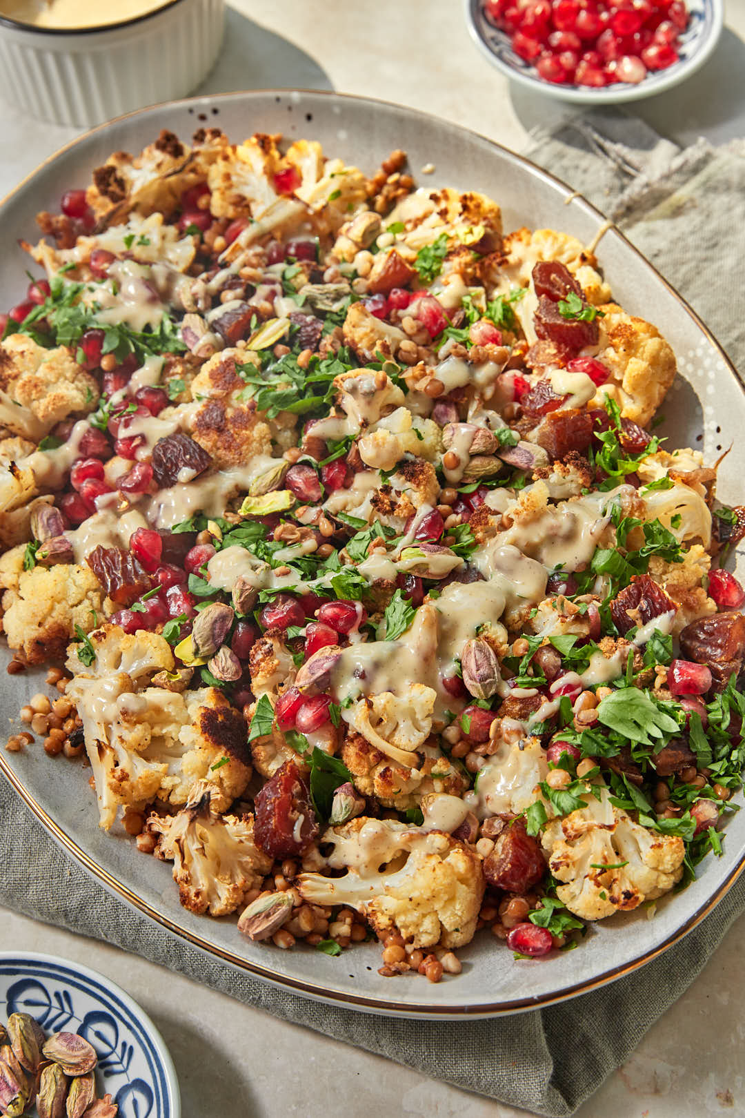 a large serving platter with roasted cauliflowers, lentils, pomegranate seeds, dates, and parsley.